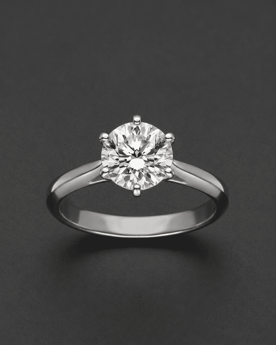 Round brilliant diamond solitaire ring with a six-prong setting in white metal, on a dark grey background
