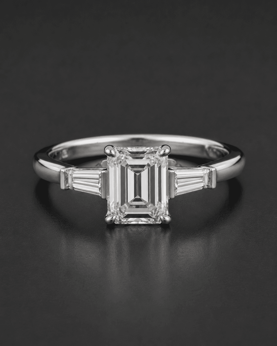 Emerald-cut diamond ring flanked by tapered baguette side stones in white metal