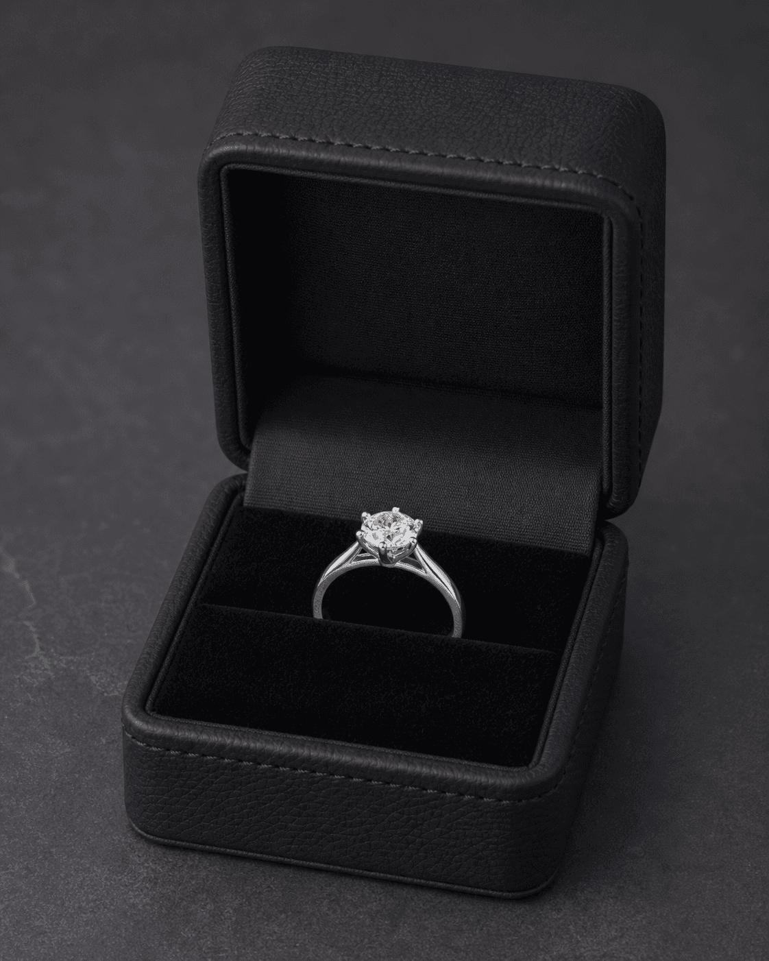 Completed diamond solitaire ring standing in an open black presentation box on a dark surface